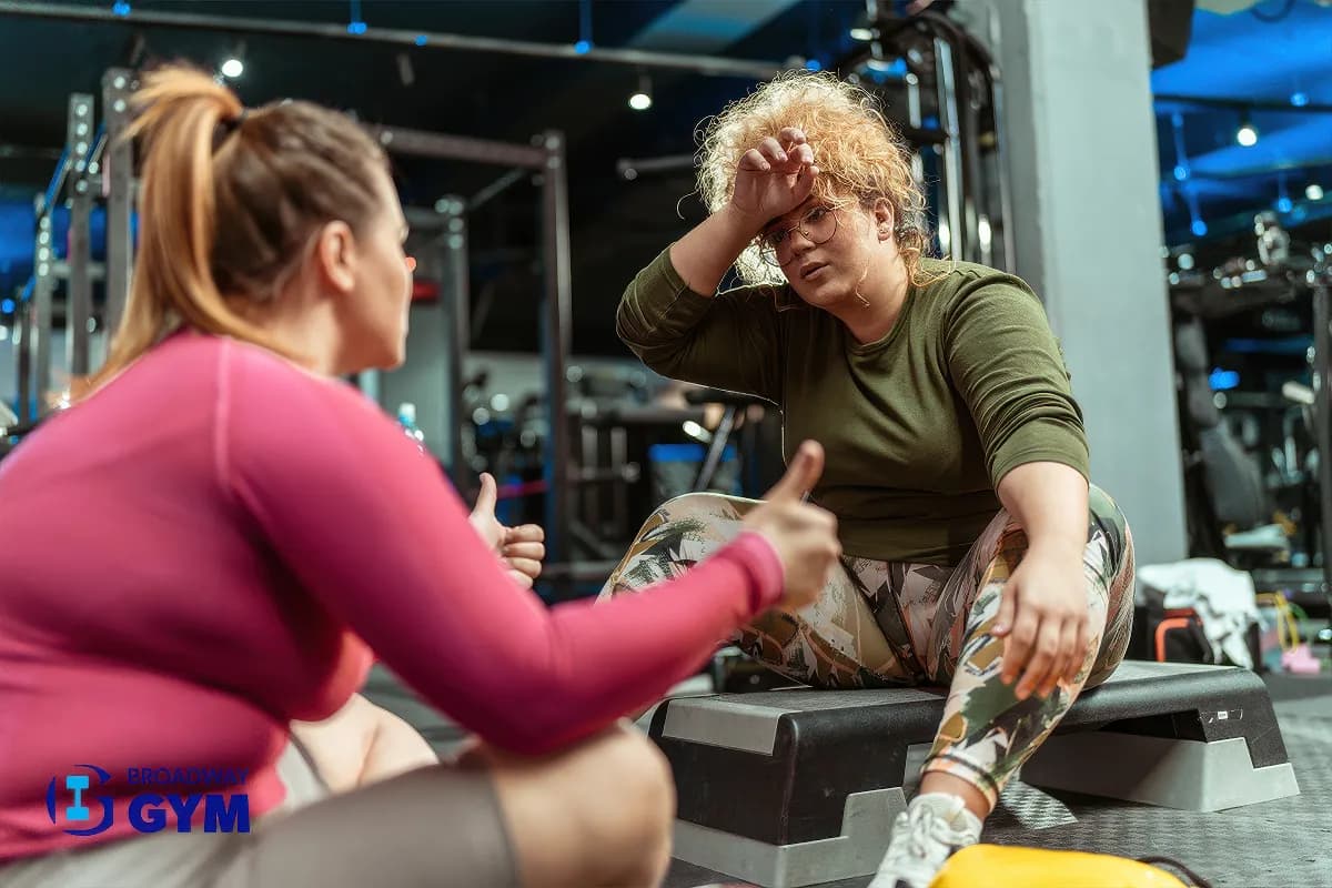 Two women embrace their bodies as they engage in a challenging workout, relaxing and talking after workout